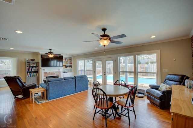 dining space with light wood-style flooring, ornamental molding, french doors, a brick fireplace, and recessed lighting