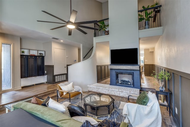 living room featuring a fireplace, visible vents, a towering ceiling, ceiling fan, and wood finished floors