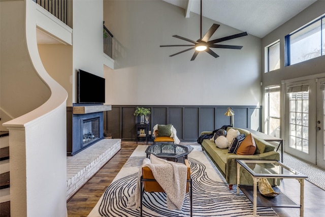 living area featuring a wainscoted wall, a fireplace, a decorative wall, wood finished floors, and high vaulted ceiling