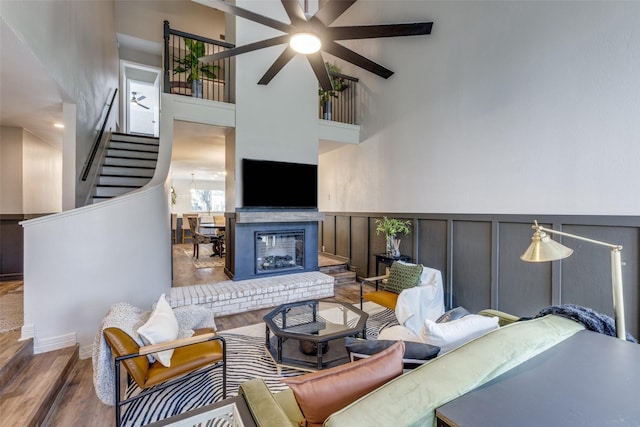 living room featuring a wainscoted wall, a fireplace, a high ceiling, wood finished floors, and stairs