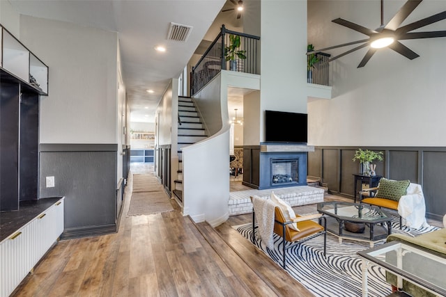 living area featuring a wainscoted wall, visible vents, a glass covered fireplace, wood finished floors, and stairs