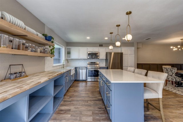 kitchen featuring stainless steel appliances, blue cabinetry, butcher block countertops, and open shelves