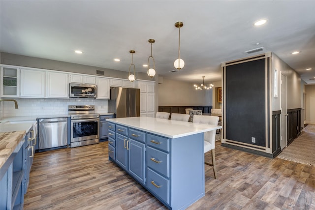 kitchen with a breakfast bar area, blue cabinets, stainless steel appliances, wood finished floors, and white cabinetry