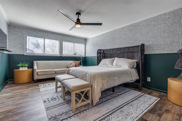 bedroom featuring a wainscoted wall, crown molding, wood finished floors, a ceiling fan, and wallpapered walls