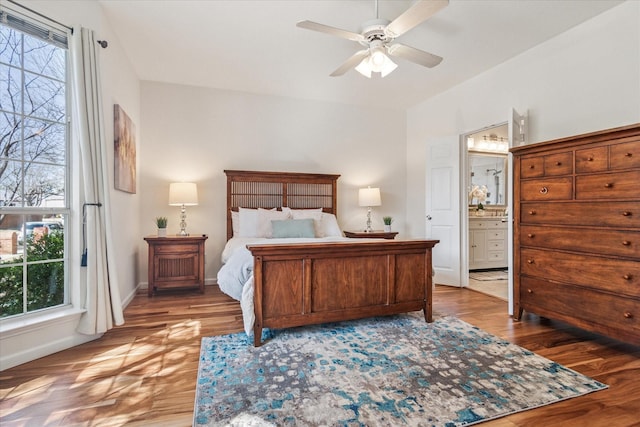 bedroom featuring a ceiling fan, wood finished floors, baseboards, and connected bathroom