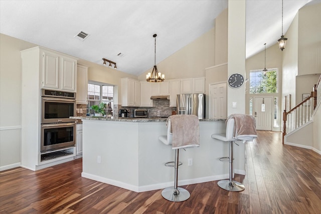 kitchen featuring dark wood-type flooring, light stone counters, visible vents, and appliances with stainless steel finishes