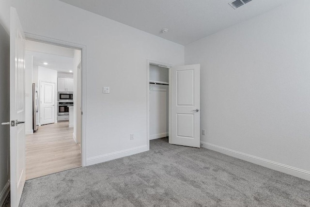 unfurnished bedroom featuring carpet, a closet, visible vents, freestanding refrigerator, and baseboards