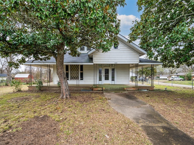 farmhouse with a shingled roof, a front lawn, a porch, and a carport