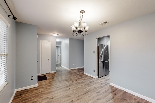 unfurnished room featuring light wood finished floors, baseboards, visible vents, and a chandelier