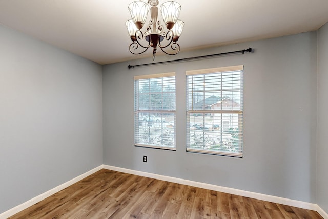 empty room with baseboards, a notable chandelier, and wood finished floors