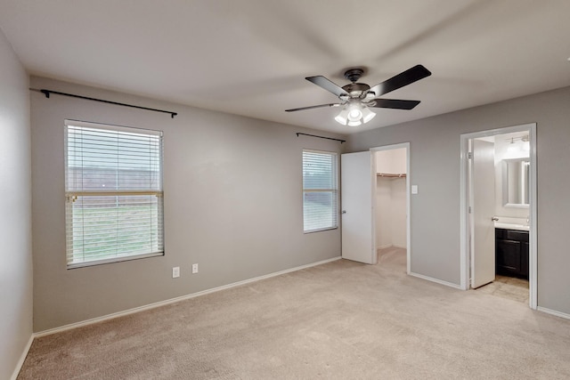 unfurnished bedroom with connected bathroom, light carpet, baseboards, a closet, and a walk in closet