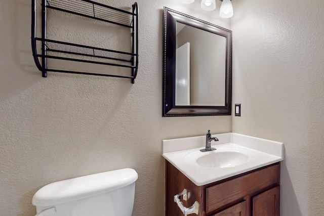 half bathroom featuring a textured wall, vanity, and toilet