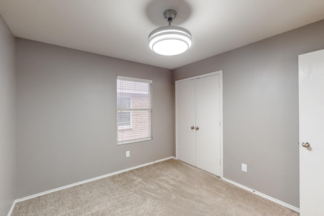 unfurnished bedroom with light carpet, baseboards, and a closet