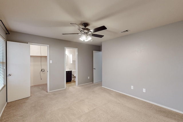 unfurnished bedroom with baseboards, a walk in closet, visible vents, and light colored carpet