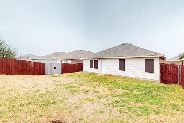 rear view of house with a shingled roof, a lawn, and a fenced backyard