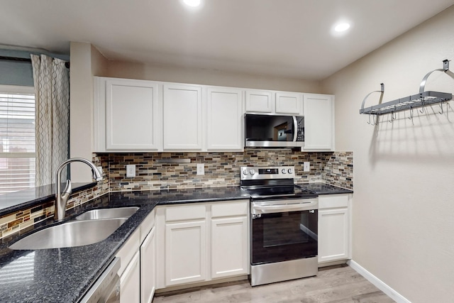 kitchen featuring stainless steel appliances, a sink, white cabinetry, decorative backsplash, and dark stone countertops