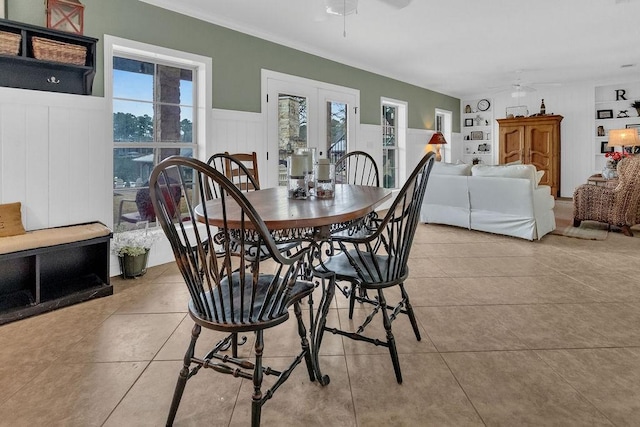 dining area with french doors, a wainscoted wall, light tile patterned floors, a decorative wall, and ceiling fan