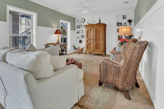 living area featuring light tile patterned floors, built in features, visible vents, a wainscoted wall, and ceiling fan