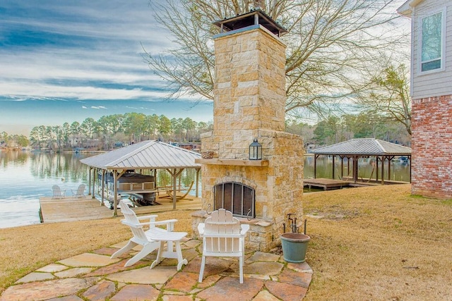 view of patio with a boat dock, a water view, an outdoor stone fireplace, and a gazebo