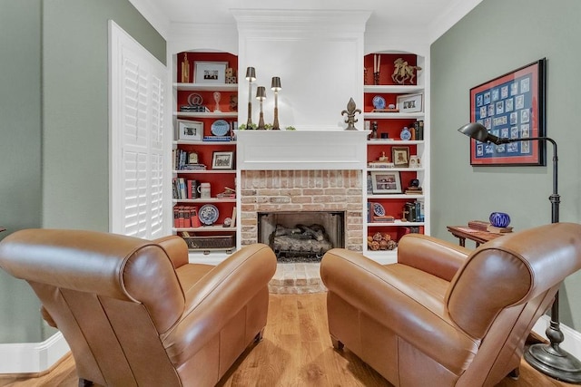 sitting room featuring ornamental molding, light wood-type flooring, a brick fireplace, and built in shelves