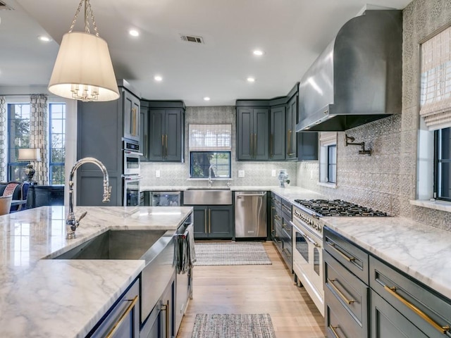 kitchen with visible vents, appliances with stainless steel finishes, a sink, wall chimney range hood, and light stone countertops