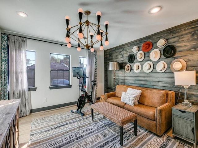 living area featuring an inviting chandelier, an accent wall, wooden walls, wood finished floors, and baseboards