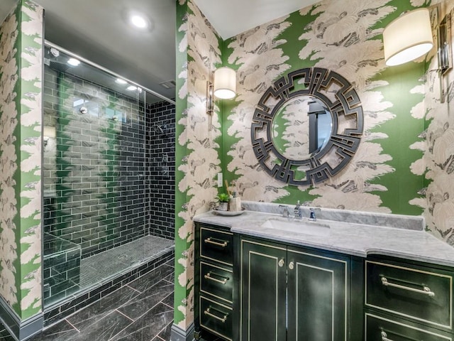 full bath featuring tiled shower, vanity, and wallpapered walls