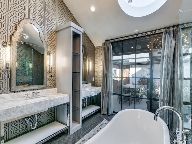 bathroom featuring two vanities, vaulted ceiling, a sink, a freestanding tub, and wallpapered walls