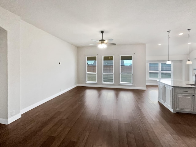 unfurnished living room with dark wood-type flooring, ceiling fan, and baseboards