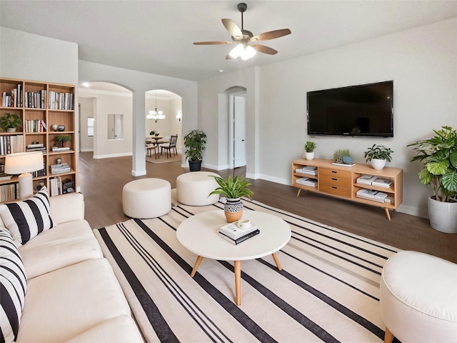 living area with arched walkways, ceiling fan with notable chandelier, wood finished floors, and baseboards