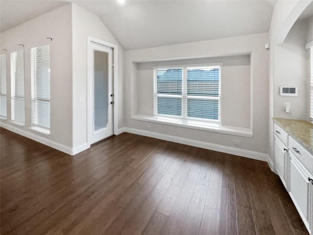 unfurnished dining area with dark wood finished floors, vaulted ceiling, and baseboards