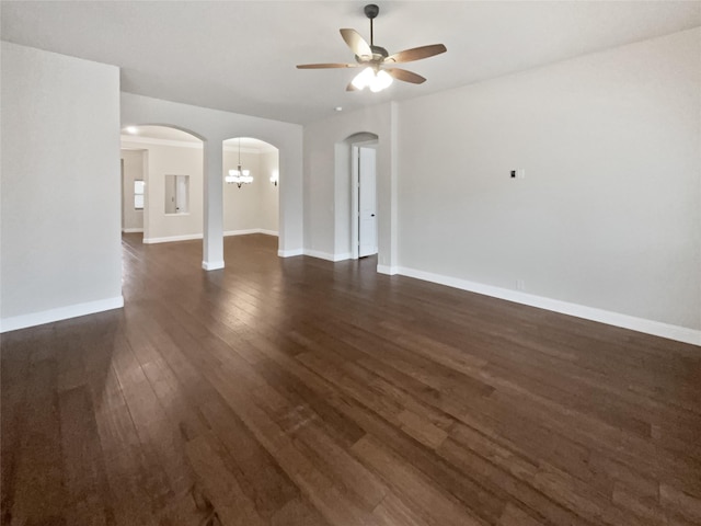 unfurnished living room featuring baseboards, arched walkways, dark wood-type flooring, and ceiling fan with notable chandelier