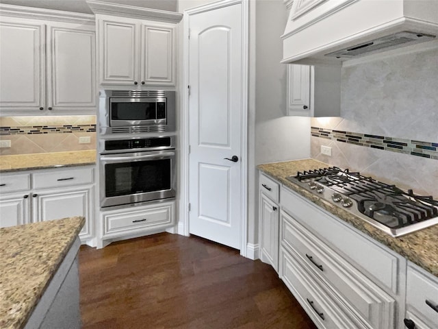 kitchen featuring appliances with stainless steel finishes, premium range hood, decorative backsplash, and white cabinetry