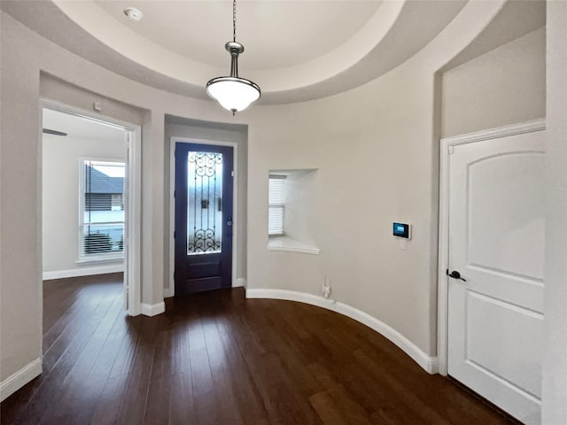 entryway with wood-type flooring, a tray ceiling, and baseboards