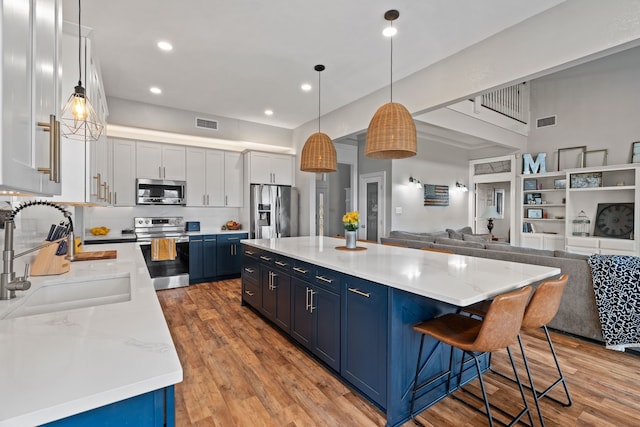 kitchen with light wood finished floors, appliances with stainless steel finishes, open floor plan, blue cabinets, and a sink