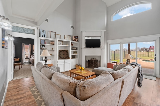 living room with visible vents, a fireplace, a high ceiling, and wood finished floors