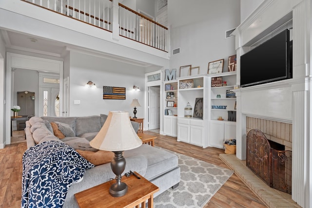 living room with light wood-style floors, a brick fireplace, visible vents, and a towering ceiling