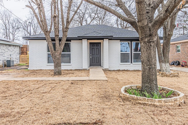 ranch-style house featuring central air condition unit, roof with shingles, and brick siding