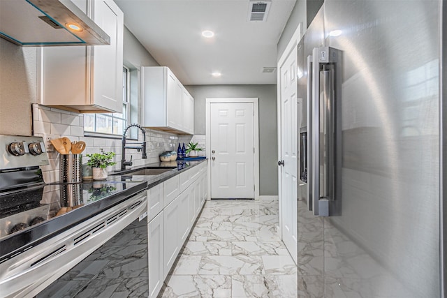 kitchen featuring marble finish floor, appliances with stainless steel finishes, white cabinets, a sink, and wall chimney exhaust hood