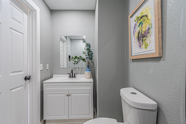 half bath with toilet, vanity, and a textured wall