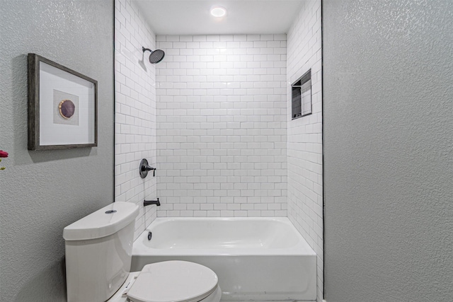 bathroom with a textured wall, bathing tub / shower combination, and toilet