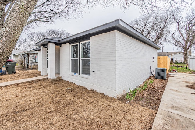 view of property exterior featuring brick siding, fence, and central air condition unit