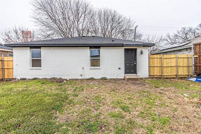 back of house featuring brick siding, fence, and a lawn