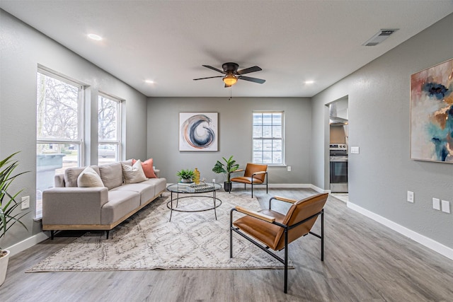 living room featuring a ceiling fan, visible vents, baseboards, and wood finished floors