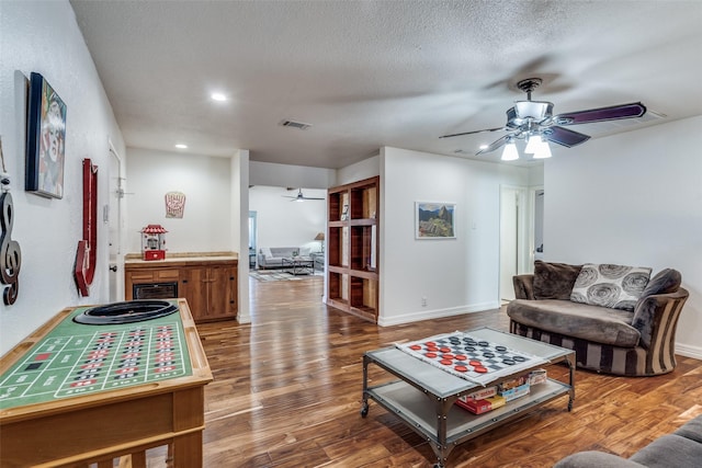 living room with a ceiling fan, a textured ceiling, baseboards, and wood finished floors