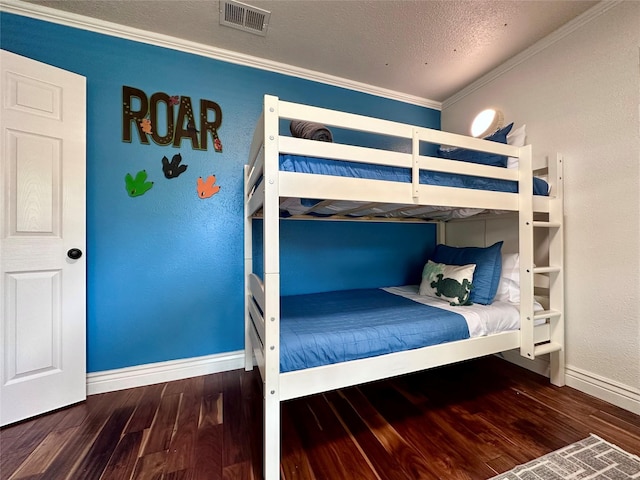 bedroom featuring visible vents, ornamental molding, a textured ceiling, wood finished floors, and baseboards