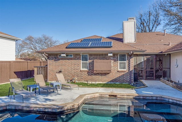 rear view of house featuring a patio, brick siding, a fenced in pool, and roof mounted solar panels