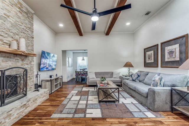 living room with a stone fireplace, wood finished floors, visible vents, beamed ceiling, and crown molding