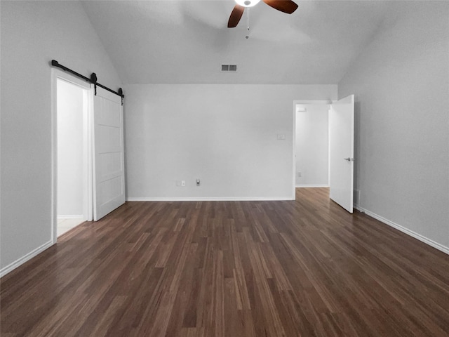 unfurnished bedroom featuring a barn door, dark wood-type flooring, visible vents, baseboards, and vaulted ceiling