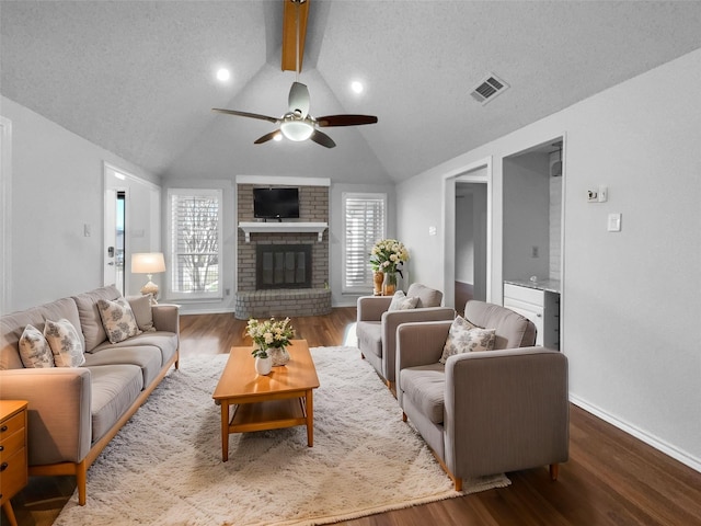 living area featuring visible vents, lofted ceiling with beams, ceiling fan, wood finished floors, and a fireplace